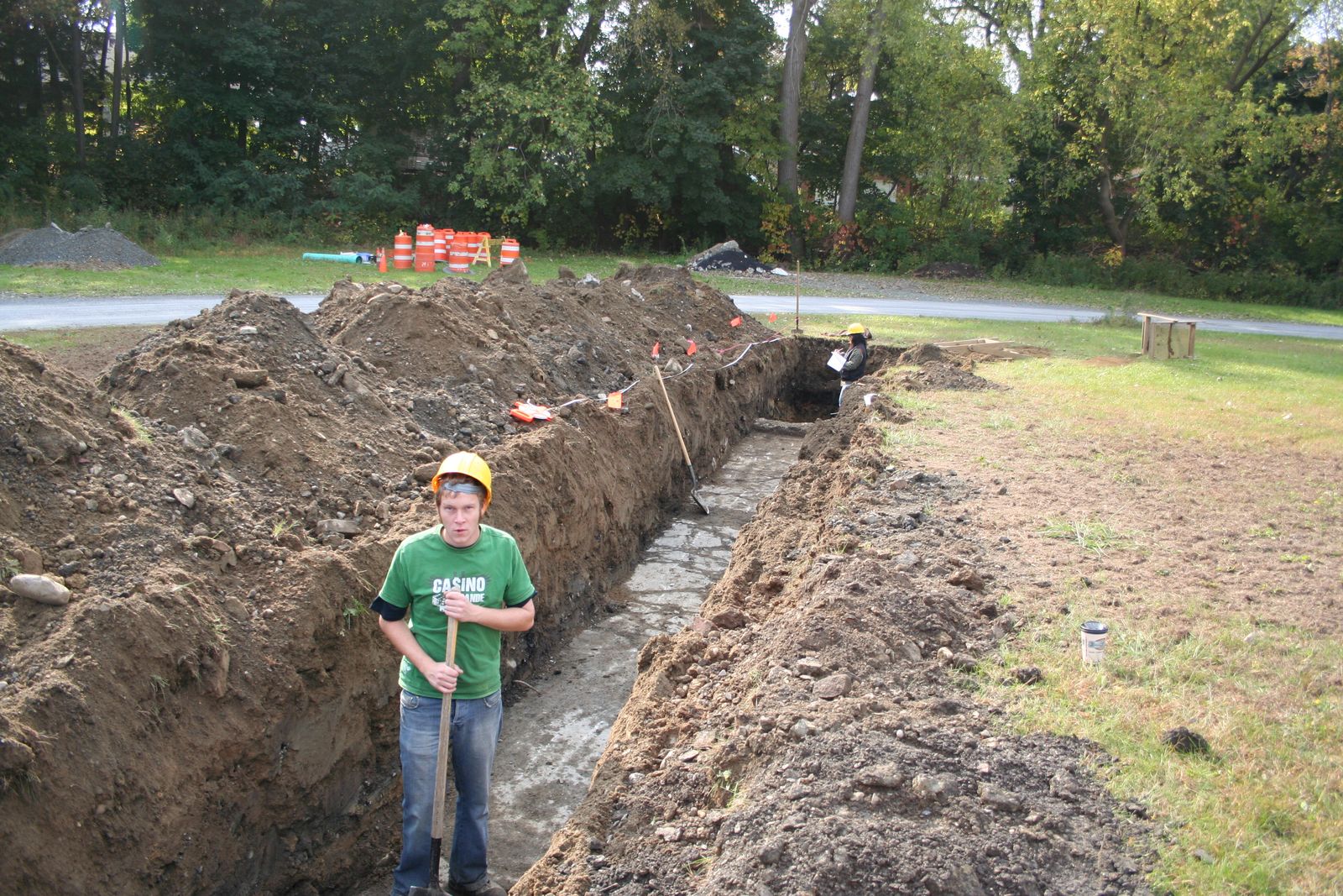 Archaeologist standing in a long machine-cut trench during a site examination
