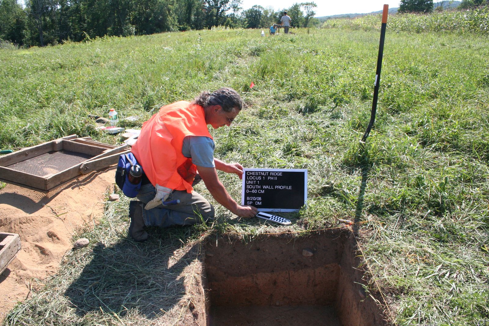 Archaeologist recording a test unit with a laptop in an open field